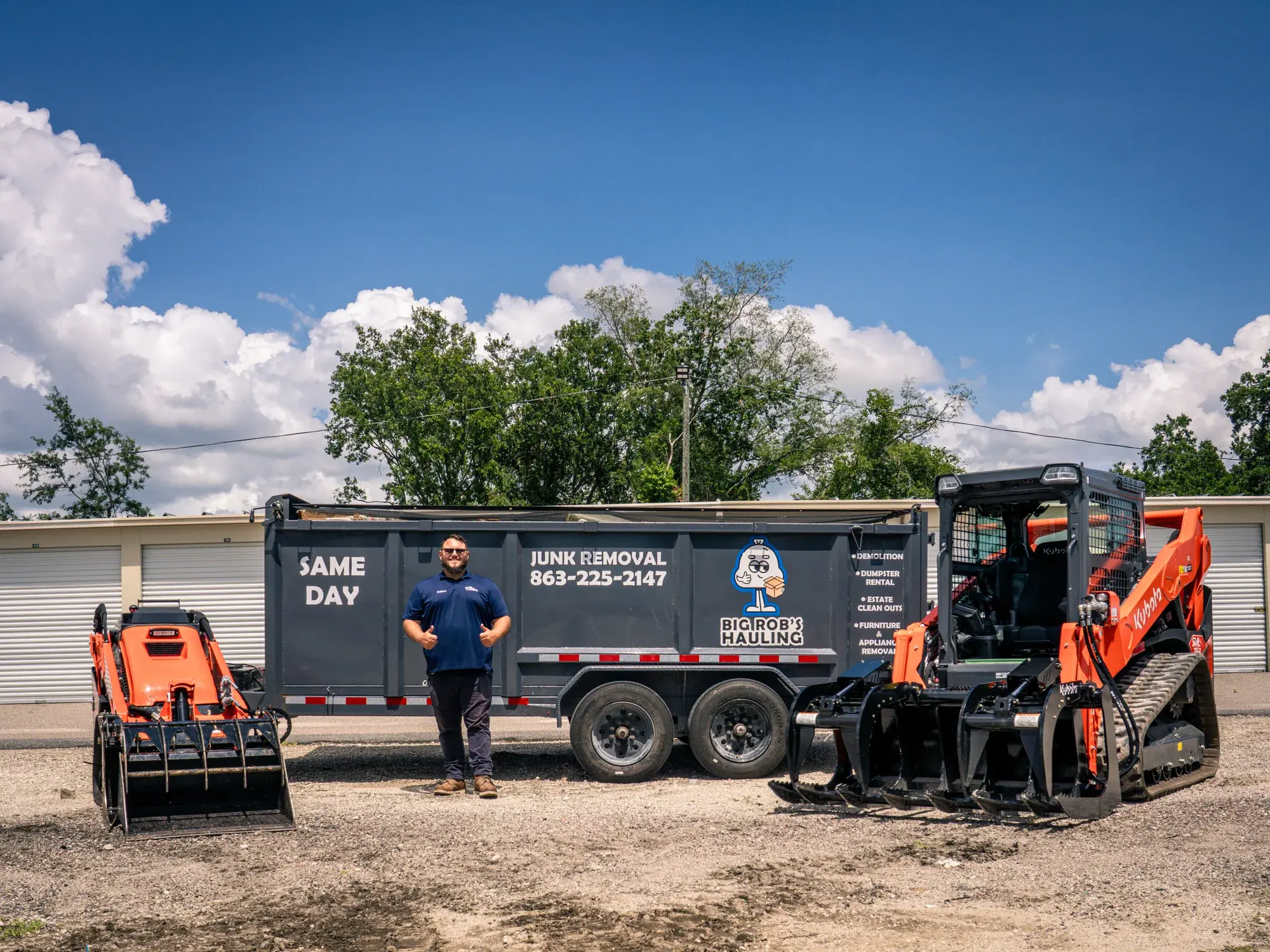 Rob of Big Rob's Hauling standing between the Same Day dump trailer and two Kubota skid steers in Davenport, FL