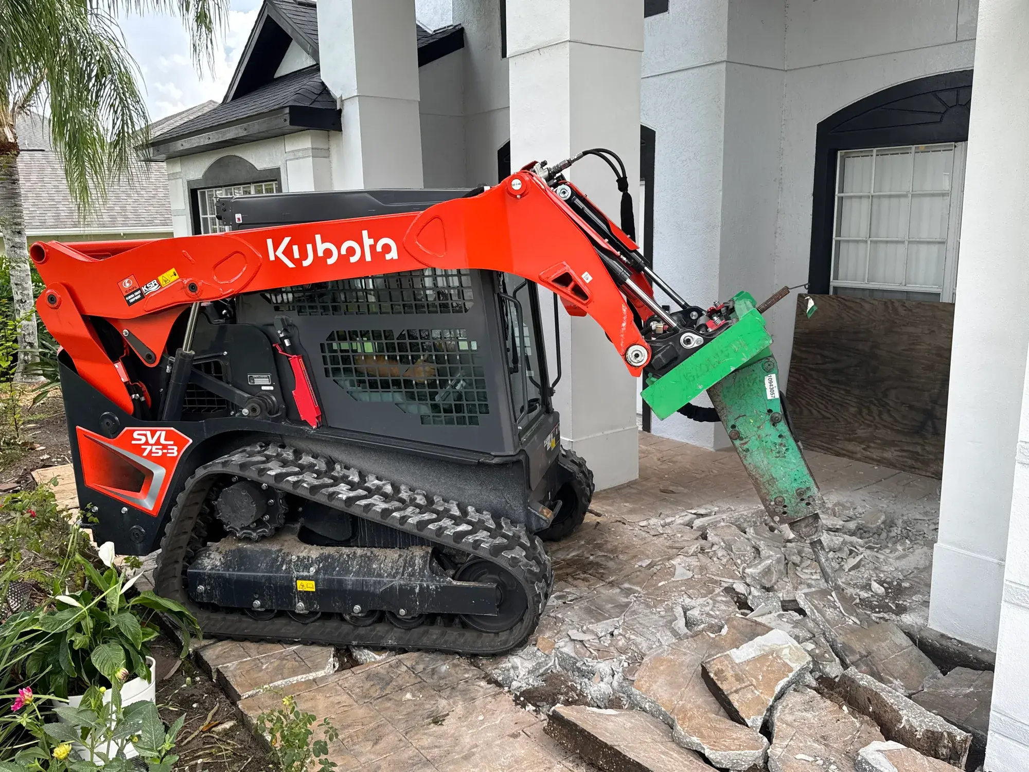 Kubota skid steer with a breaker attachment breaking up a concrete patio in Polk County, FL
