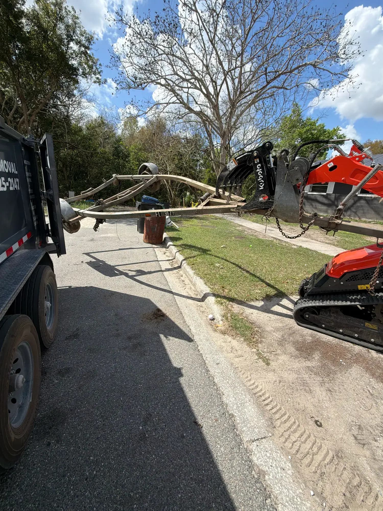 Big Rob's Hauling's Kubota grapple carrying an old boat trailer to the dump trailer on a Central Florida street