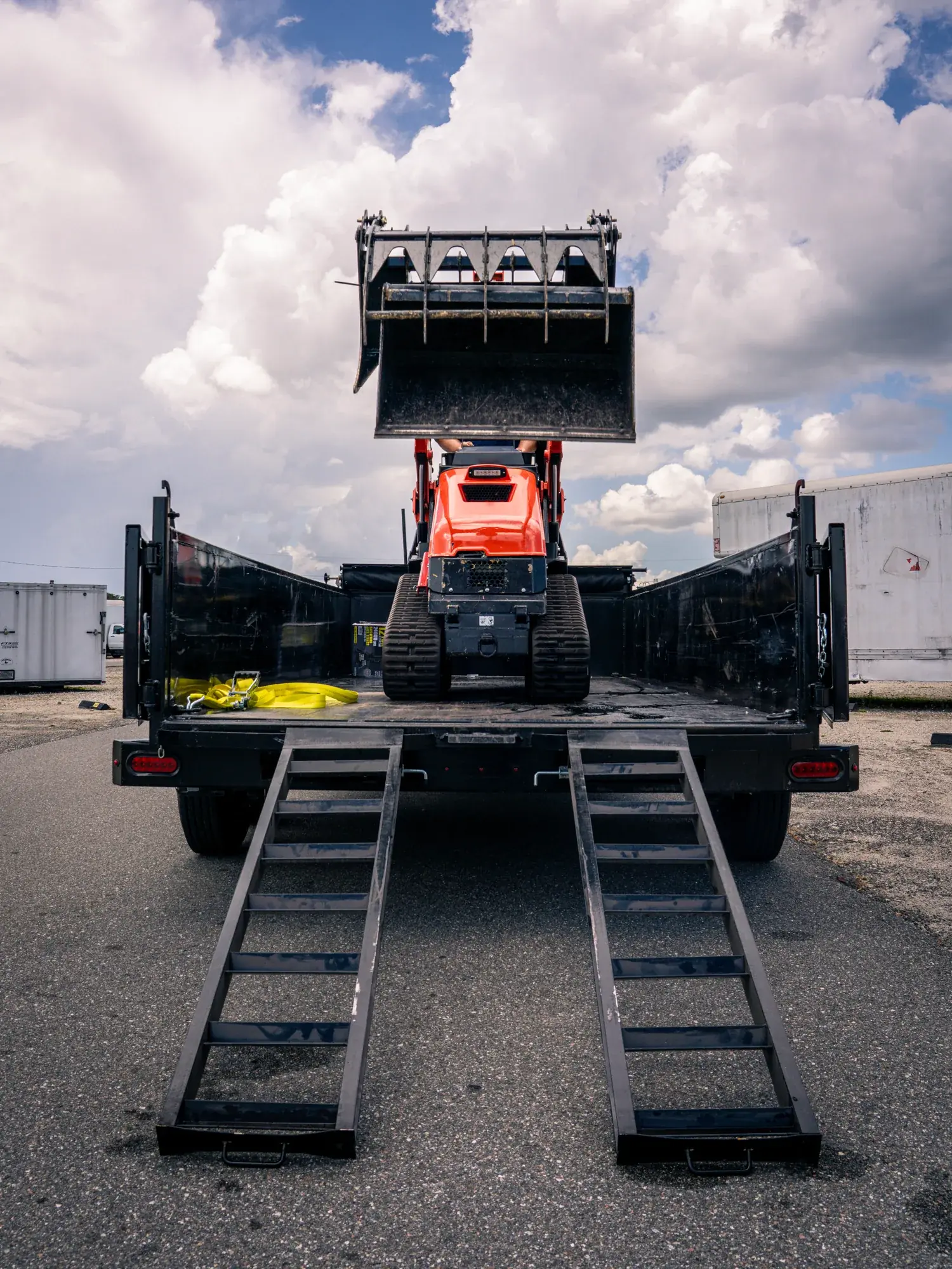 Kubota skid steer driving up the ramps of Big Rob's Hauling's flatbed trailer in Davenport, FL