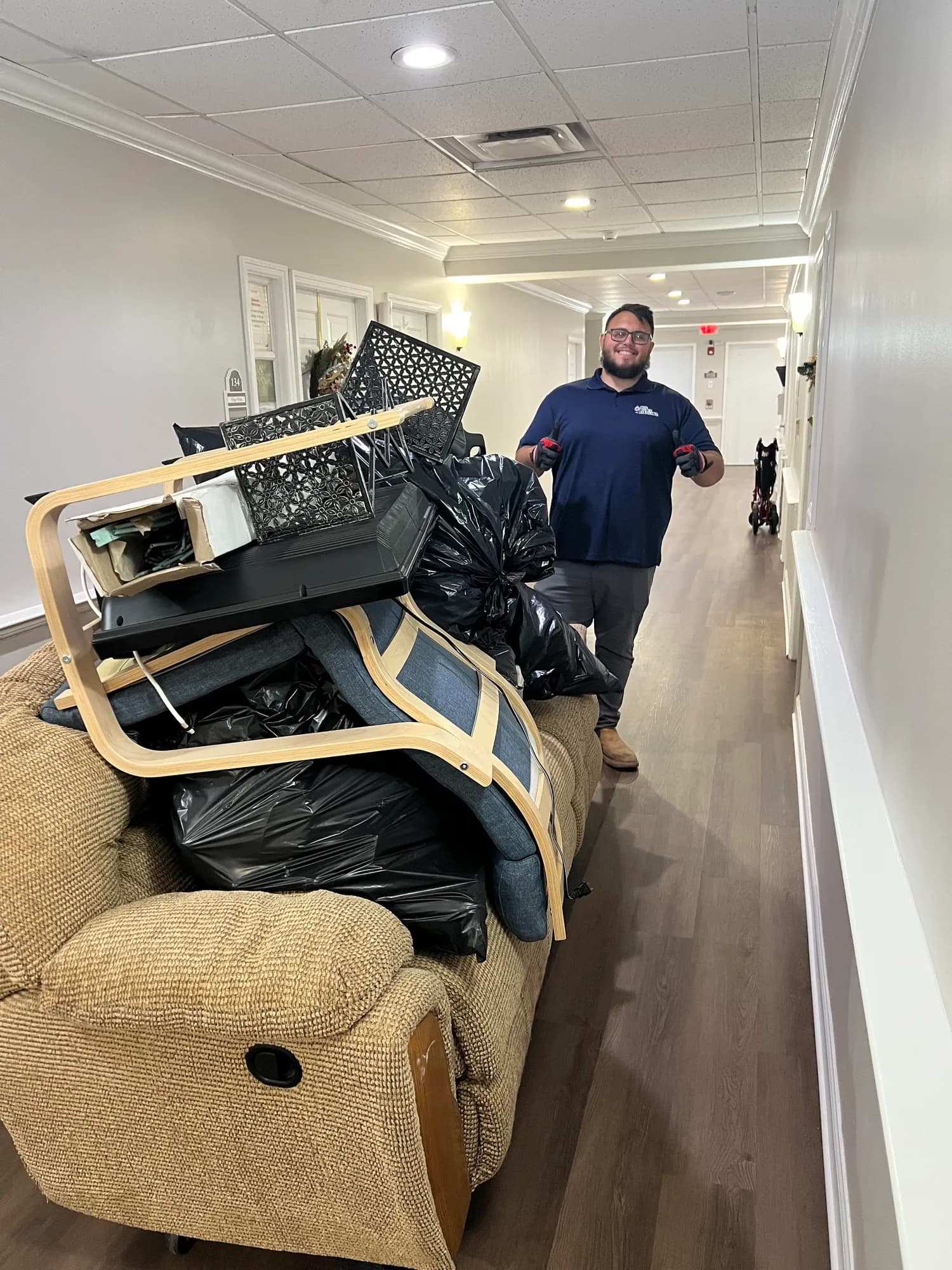 Big Rob's Hauling crew member hauling a recliner, chairs and bagged junk down a hallway on a Central Florida furniture removal