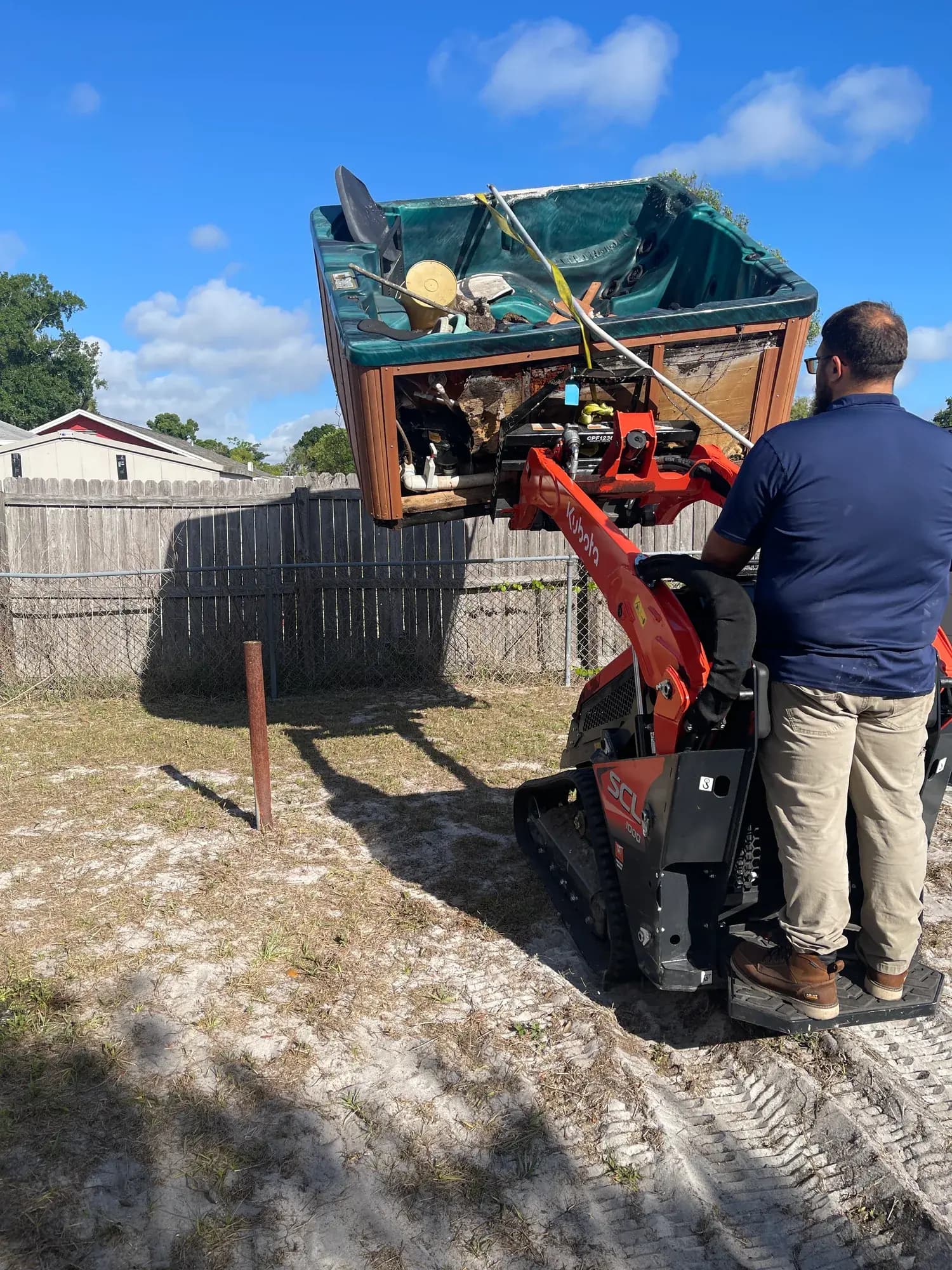 Big Rob's Hauling lifting a hot tub out whole with the mini skid steer in a Central Florida backyard
