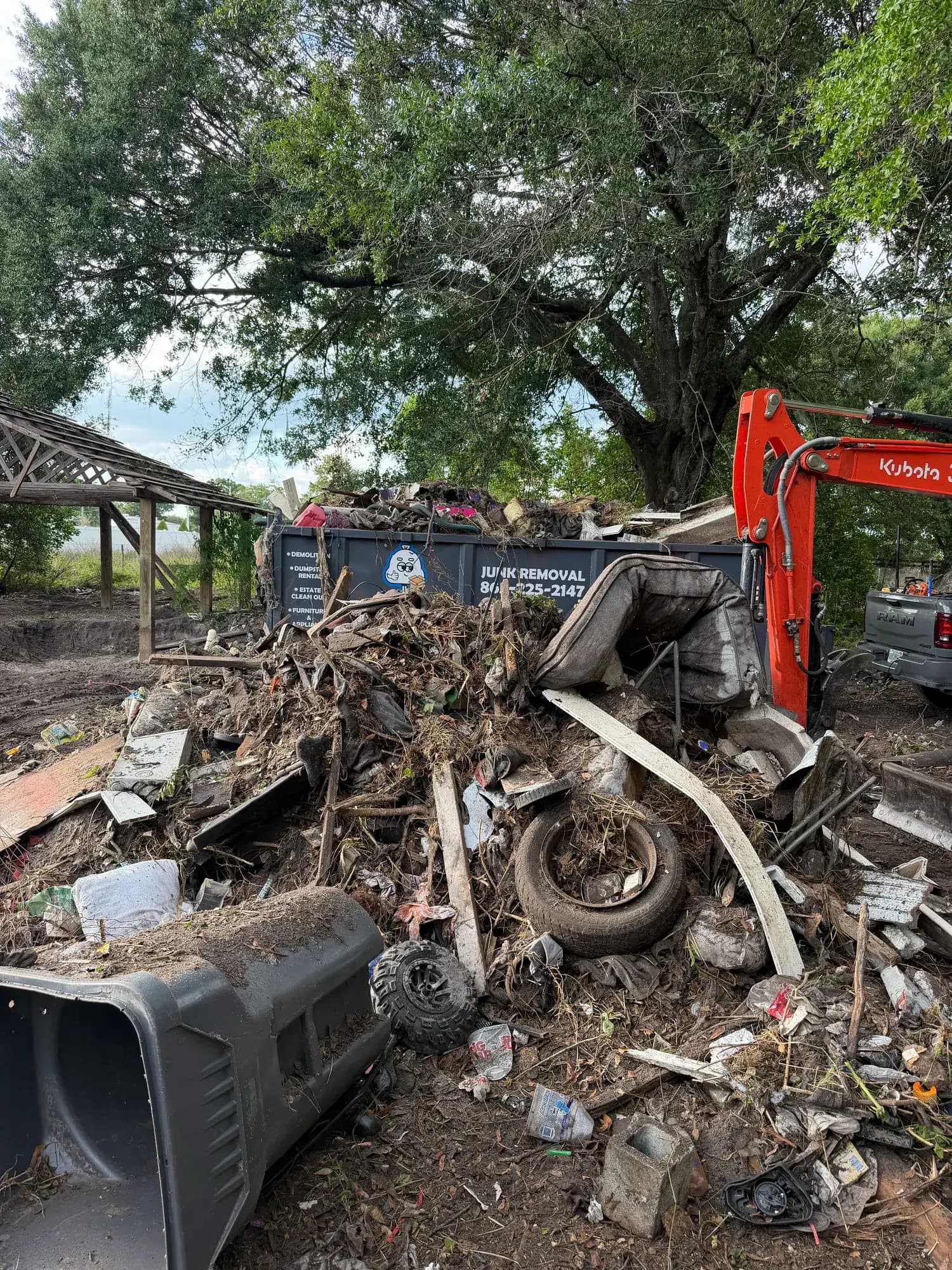 Debris pile with tires and appliances beside the Big Rob's Hauling trailer and Kubota excavator on a Lakeland, FL lot cleanout