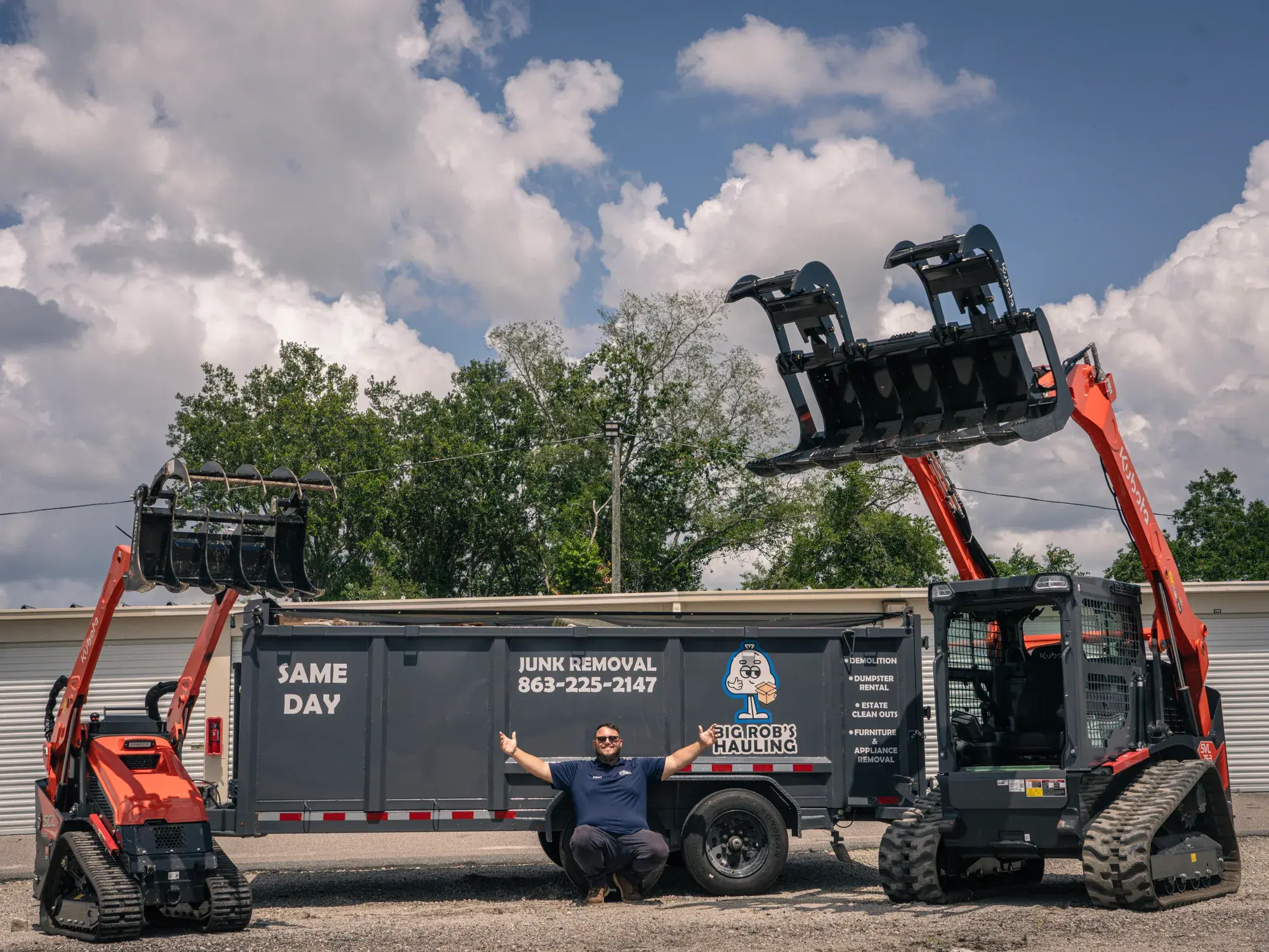 Rob kneeling arms out in front of the Big Rob's Hauling dump trailer, mini skid steer and Kubota loader in Davenport, FL