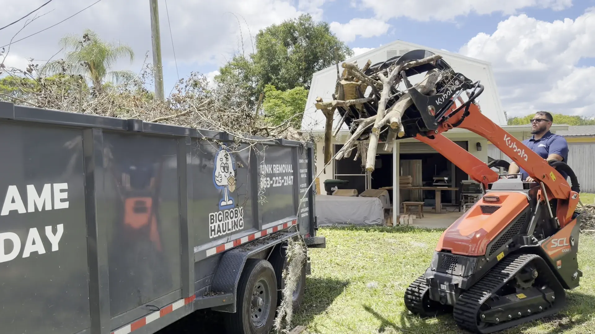 Kubota stand-on mini skid steer loading dead limbs and brush into a Big Rob's Hauling dump trailer in Orlando, FL